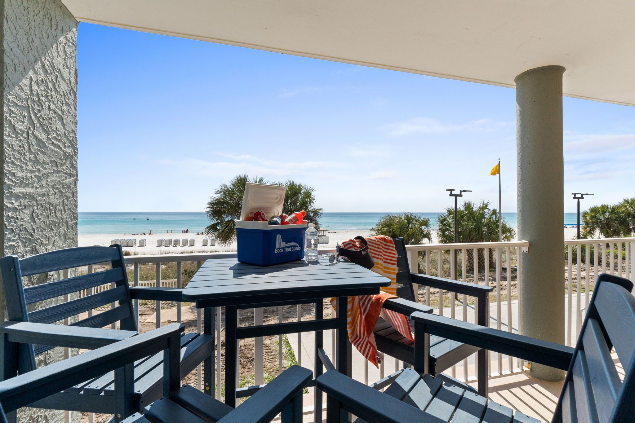 A balcony with a table, chairs, a cooler, and a beach view.