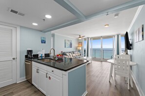 A kitchen with a large island, a dining area with a white table and chairs, and a view of the ocean through large windows. - Long Beach by Book That Condo (Panama City Beach)