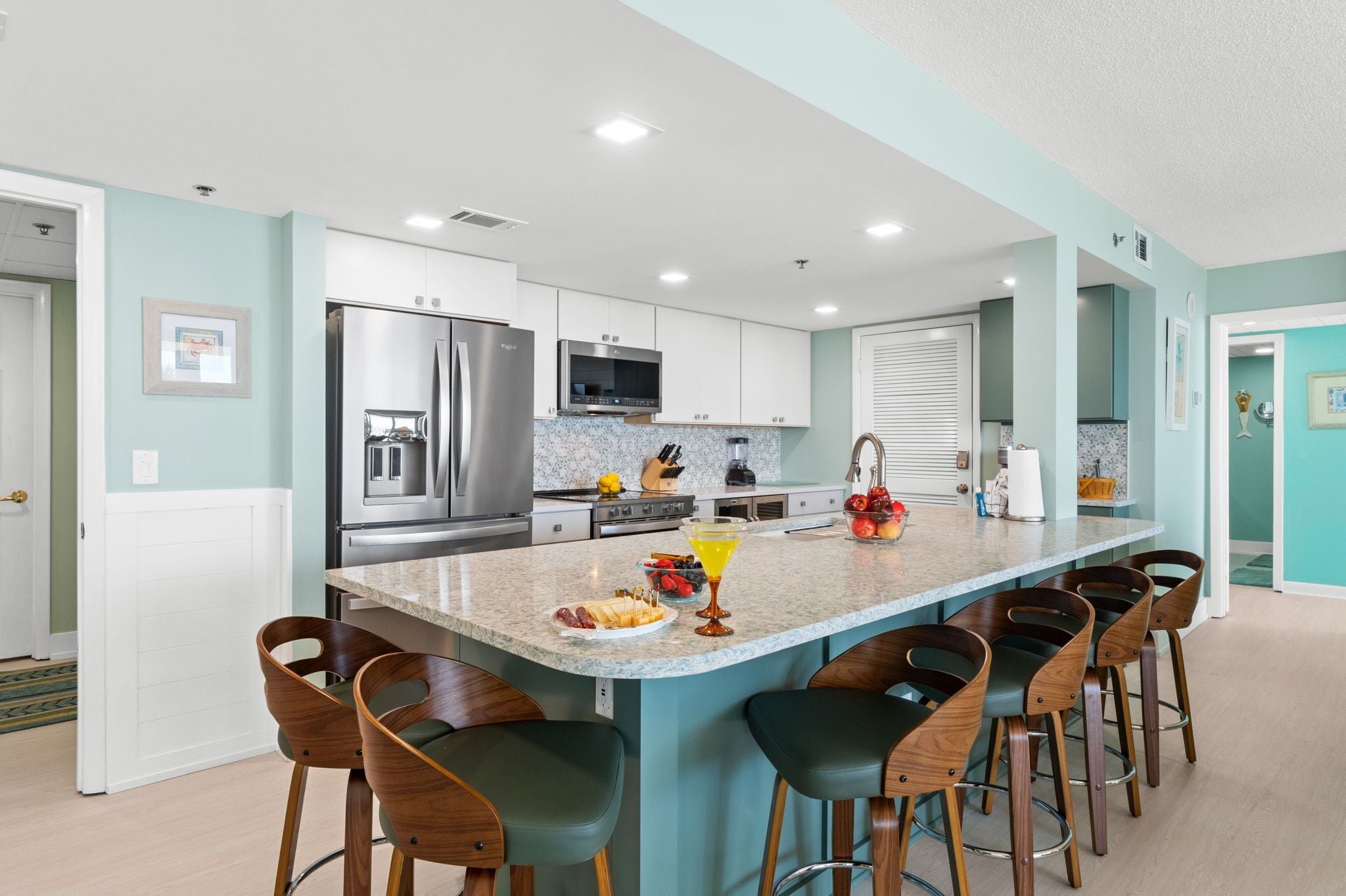 A modern kitchen with a central island, bar stools, stainless steel appliances, and a tiled backsplash.