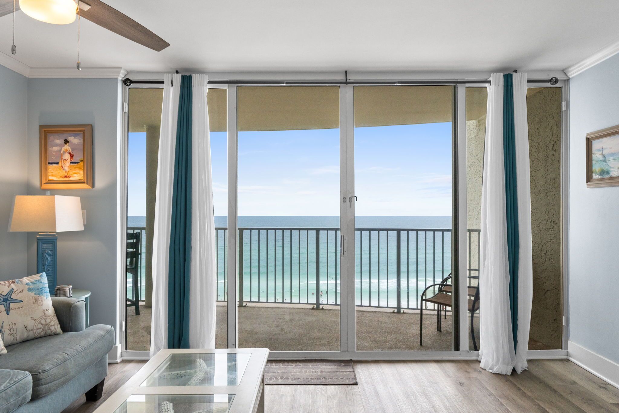 A room with a view of the ocean, a sliding glass door, a sofa, a table, and a ceiling fan.