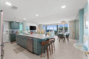 A modern kitchen with a central island, dining area with chairs, and a view through large windows. - Long Beach by Book That Condo (Panama City Beach)