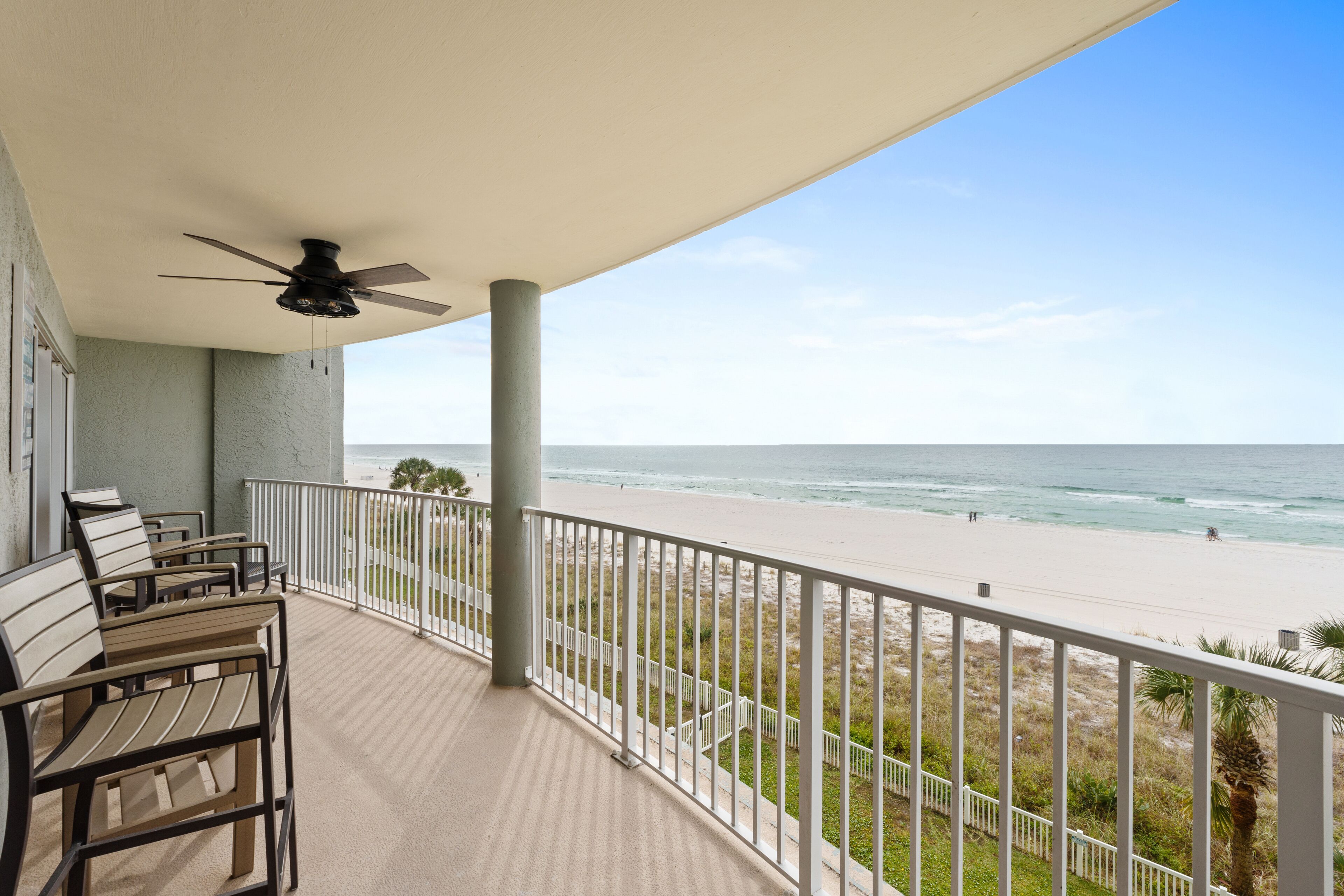 Un balcon doté d’un ventilateur de plafond, de balustrades blanches et offrant une vue sur la plage.