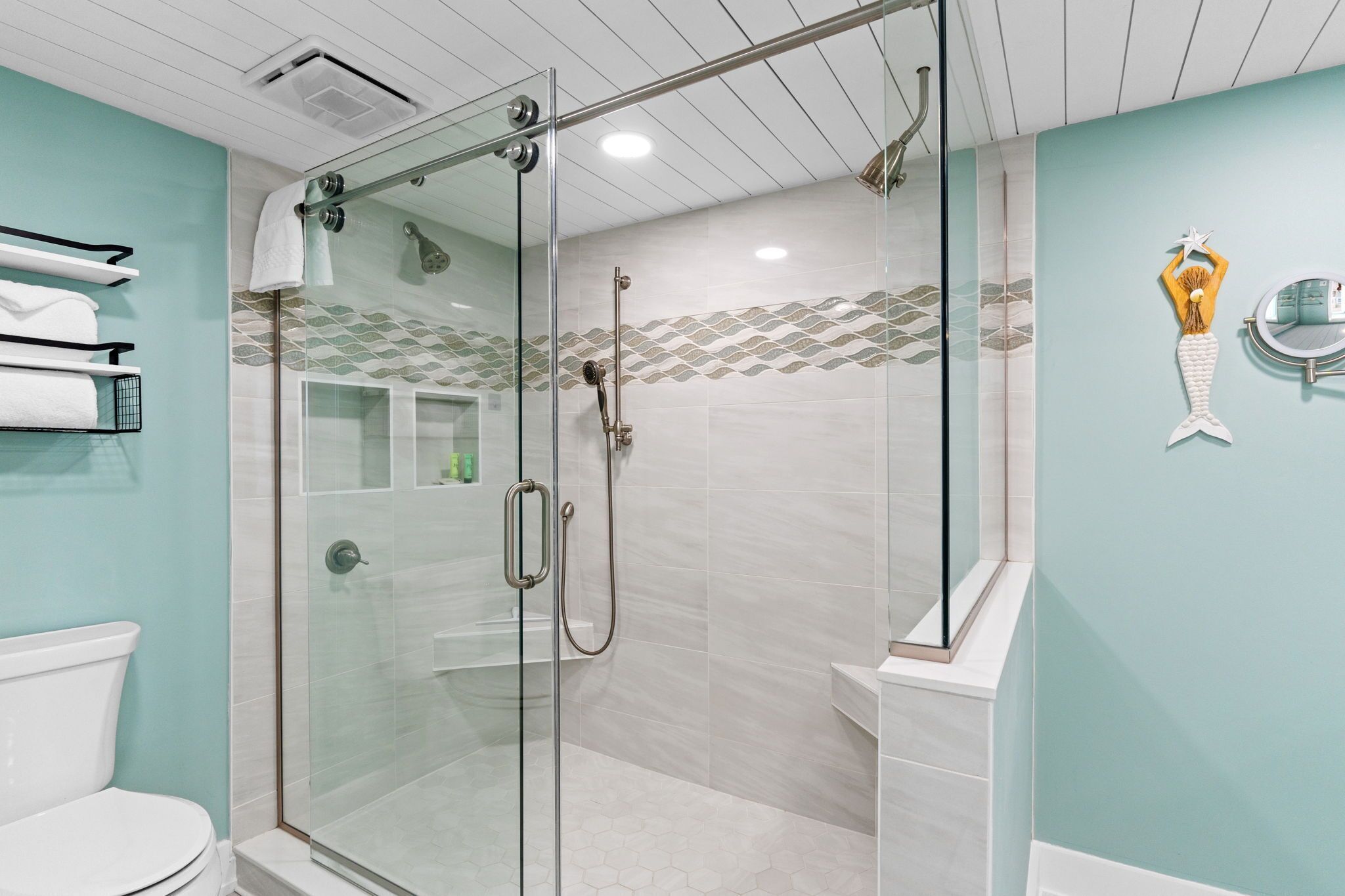 A glass-enclosed shower with a handheld showerhead, a glass door, and a tiled floor.