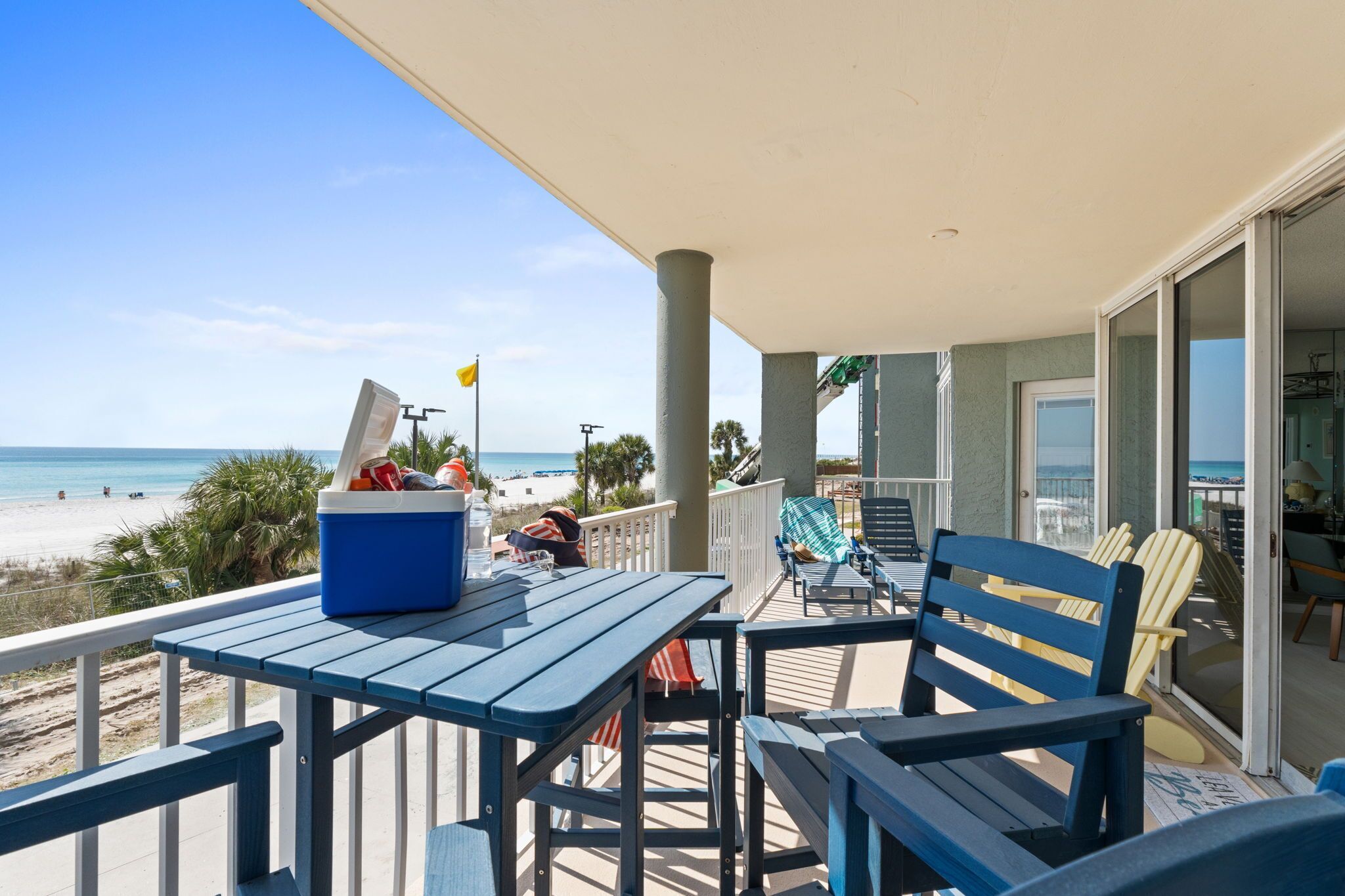 Un balcon avec une table, des chaises, une glacière et une vue sur la plage.