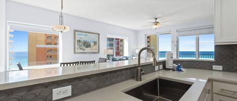 Una cocina moderna con una isla grande, un lavaplatos integrado y vistas al mar a través de las ventanas.
