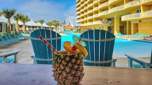 A tropical drink on a table with a pool and a Ferris wheel in the background. - Calypso Resort and Towers by Book That Condo (Panama City Beach)