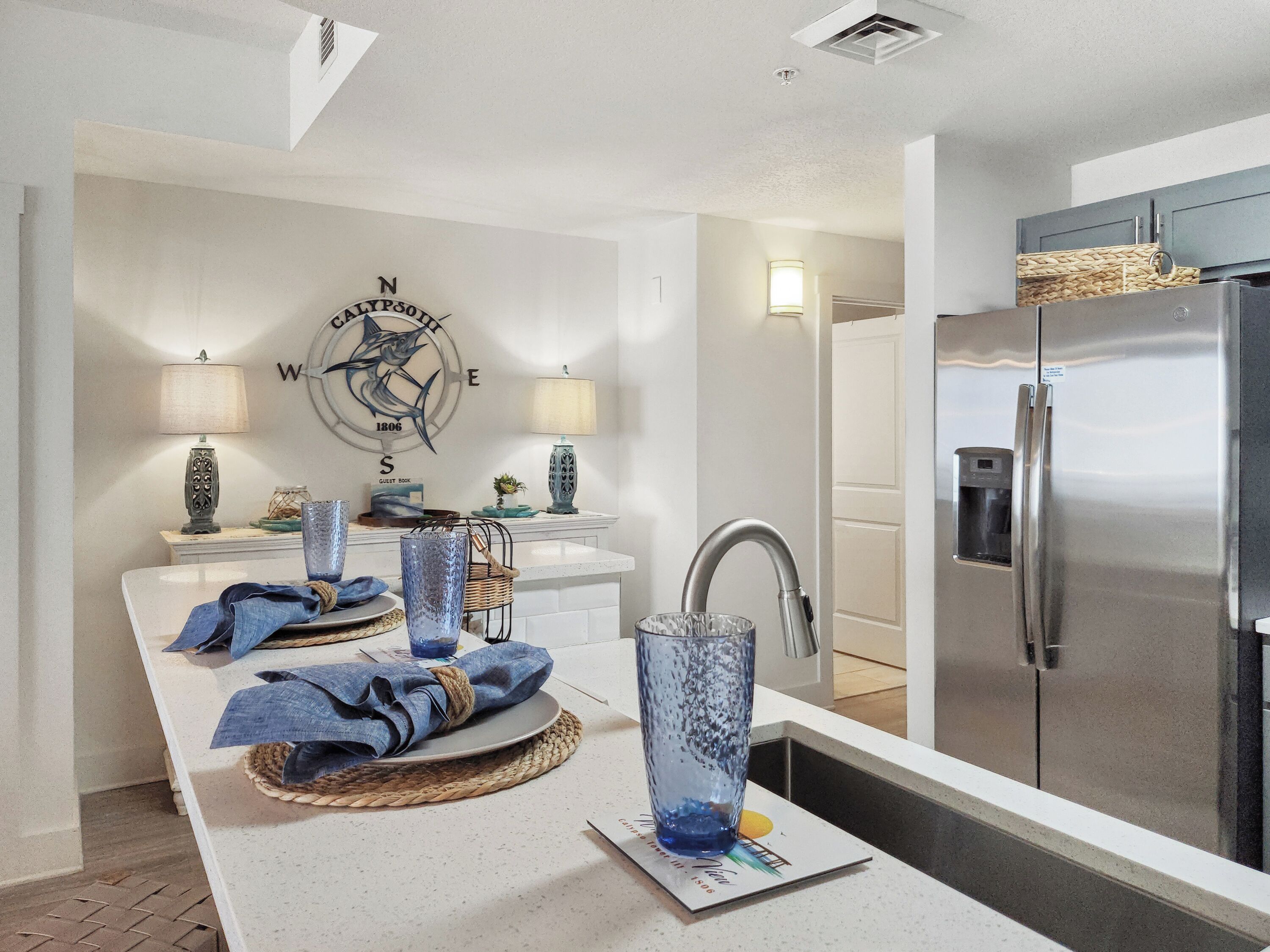 A modern kitchen with a stainless steel refrigerator, a white countertop, and a decorative wall piece.