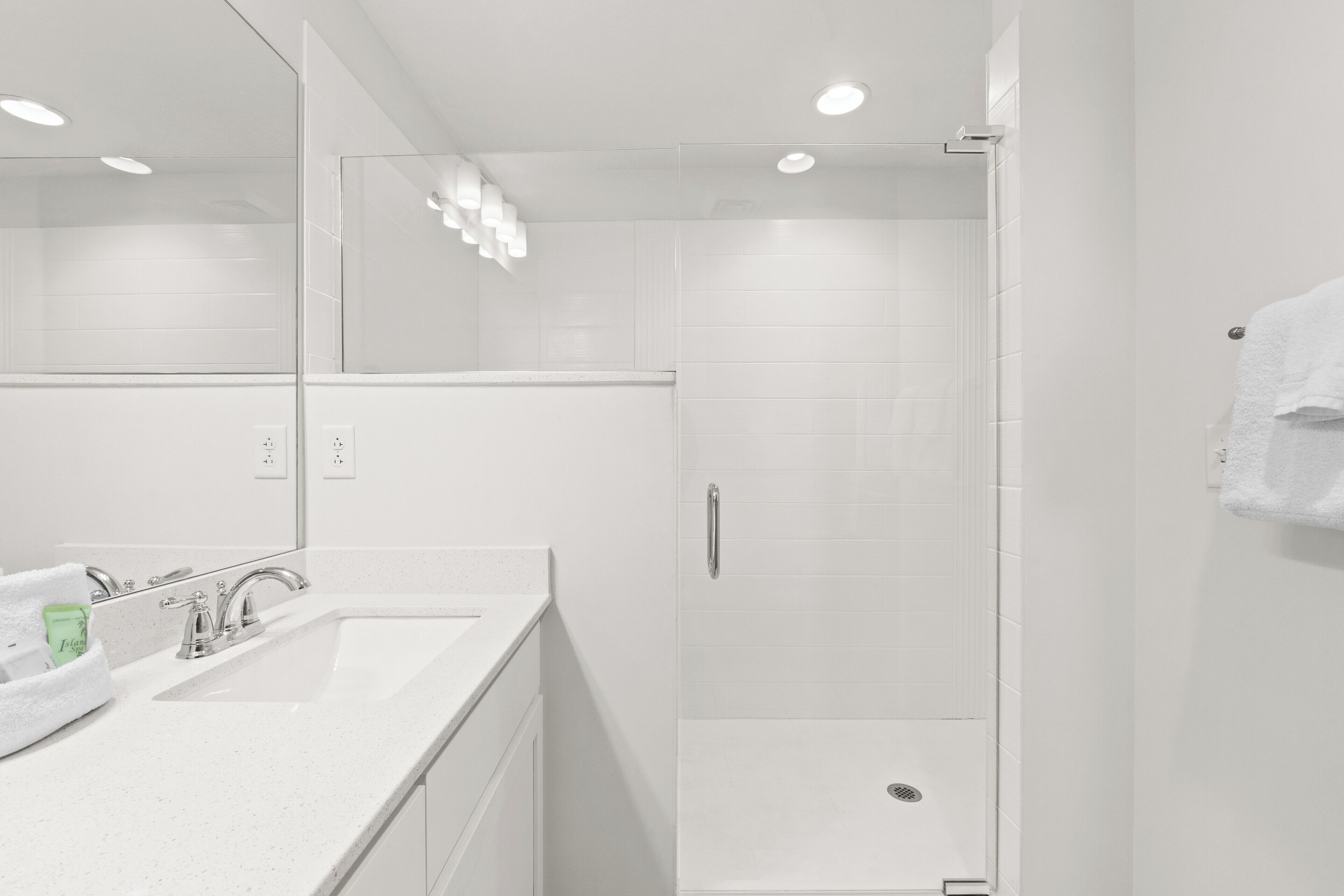 Un baño moderno con lavamanos blanco, espejo y cabina de ducha de vidrio.