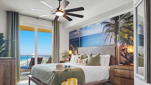 A bedroom with a bed, a nightstand, a ceiling fan, a large window with a view of the beach, and a tropical-themed wall mural. - Calypso Resort and Towers by Book That Condo (Panama City Beach)