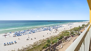 A beach with rows of blue umbrellas and lounge chairs, a pier in the background, and a clear sky. - Calypso Resort and Towers by Book That Condo (Panama City Beach)