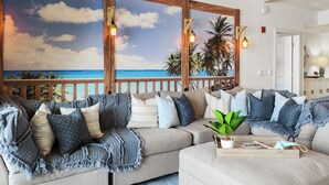 A cozy living room with a large window overlooking a beach, a wooden deck, and a modern ceiling with exposed beams. - Calypso Resort and Towers by Book That Condo (Panama City Beach)