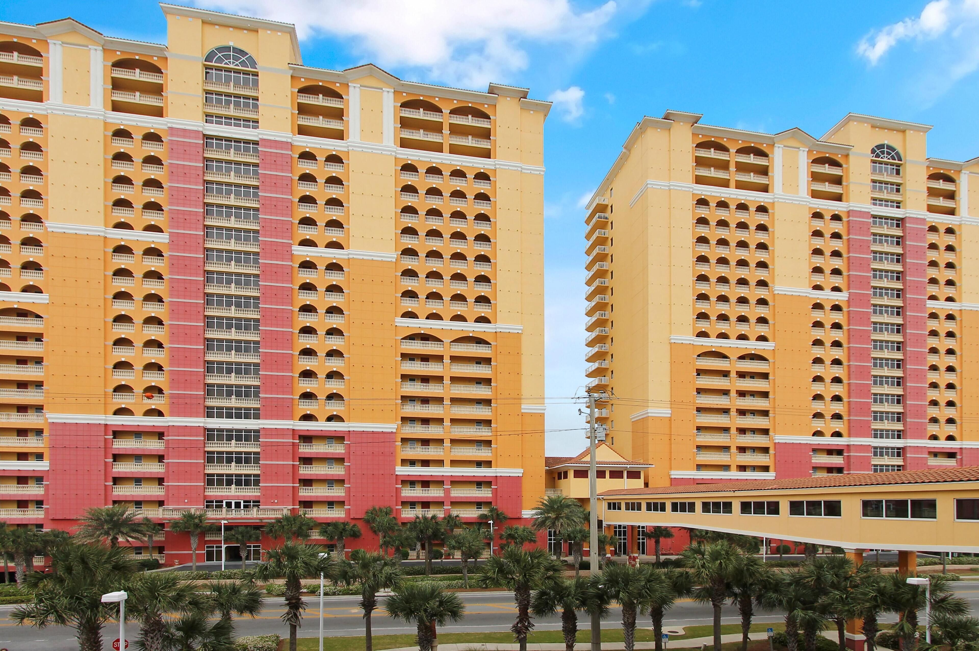 A high-rise hotel with multiple balconies, a central courtyard with palm trees, and a clear blue sky.