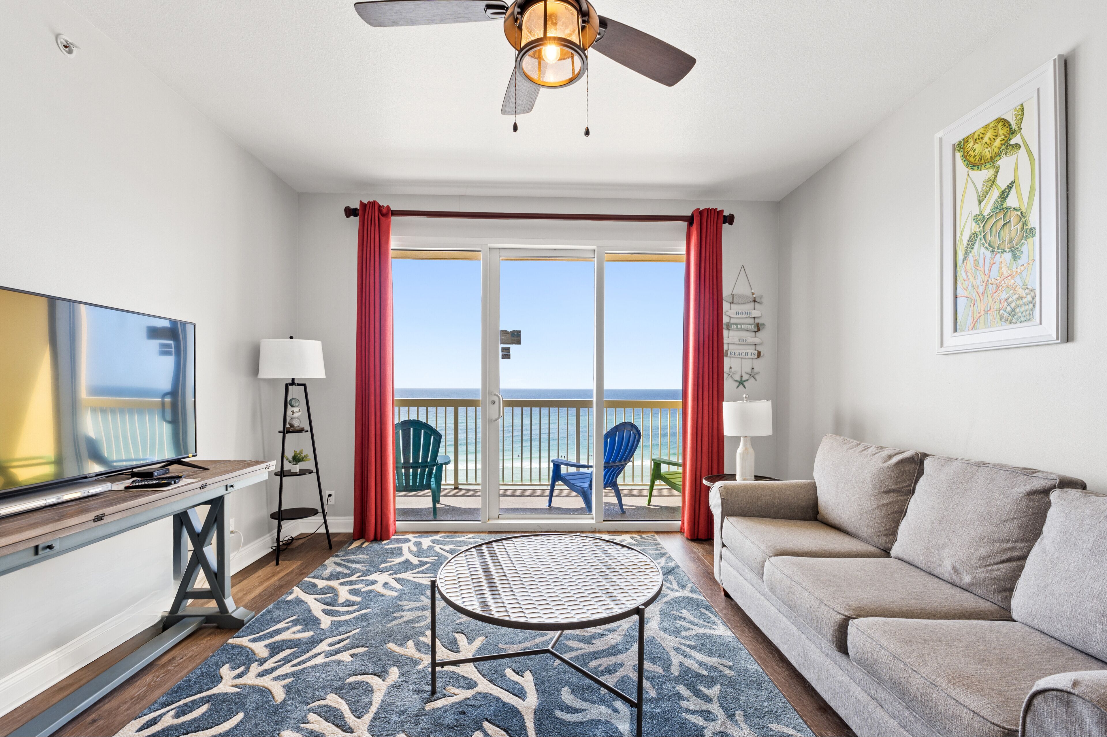 A modern living room with a television, a sofa, a coffee table, and a balcony with red curtains.