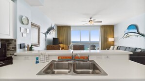 A modern kitchen with a double sink, a ceiling fan, and a view of the ocean through large windows. - Celadon Beach Resort by Book That Condo (Panama City Beach)