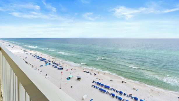 A beach with rows of blue umbrellas and lounge chairs, a sandy shore, and the ocean. - Celadon Beach Resort by Book That Condo (Panama City Beach)
