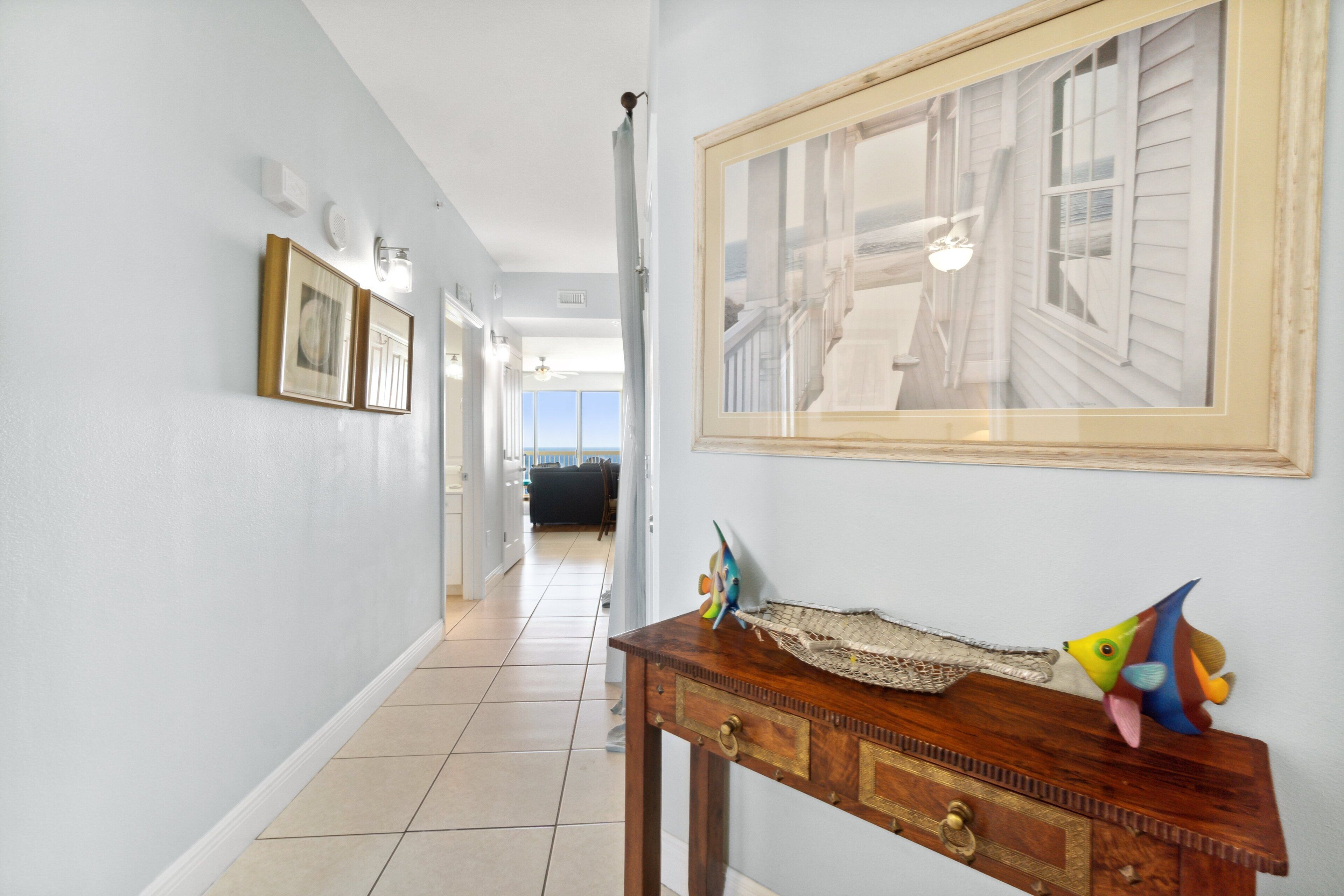 A hallway with a wooden console table, framed artwork, and a view into another room.
