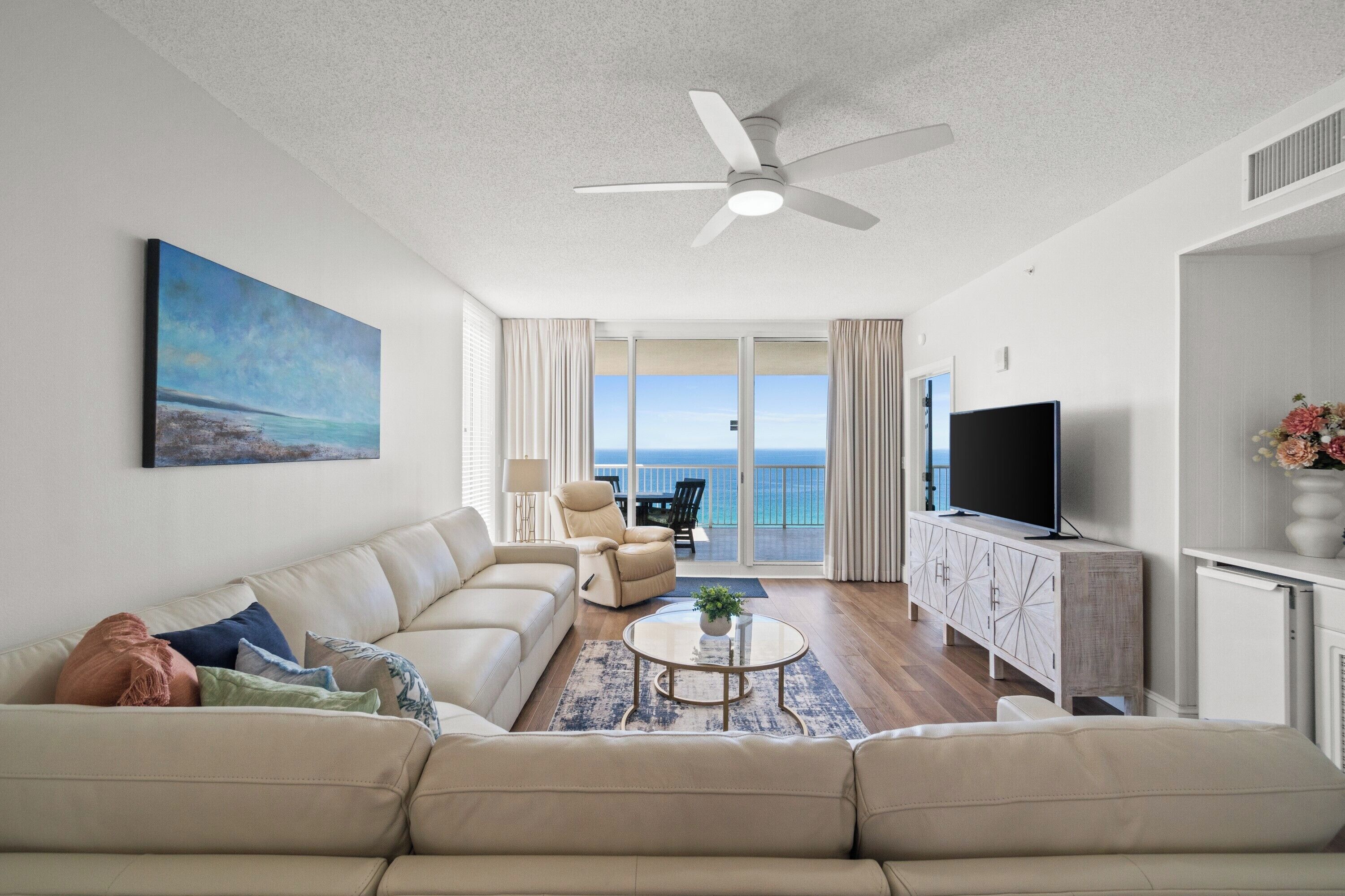 Een moderne woonkamer met een bank, een salontafel, een televisie en een balkon met uitzicht op zee.