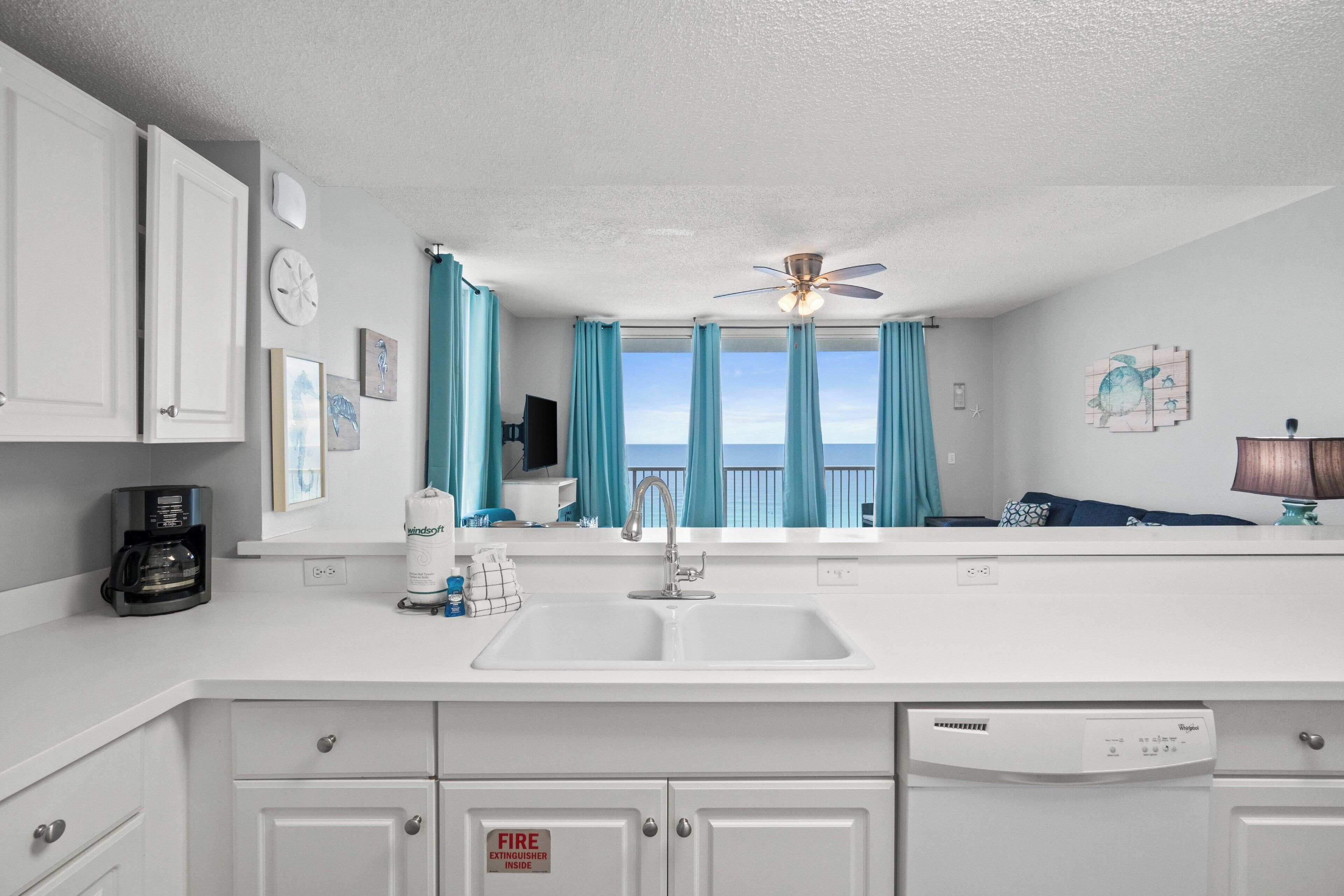 A kitchen with white cabinets, a double sink, a coffee maker, and a dishwasher.