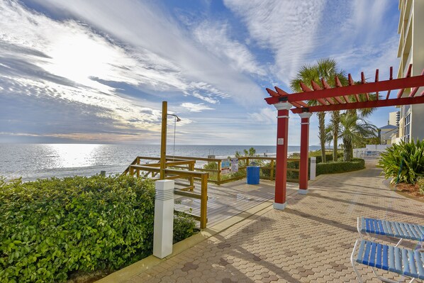 A seaside walkway with a wooden pergola, palm trees, and a view of the ocean. - Majestic Beach Resort by Book That Condo (Panama City Beach)
