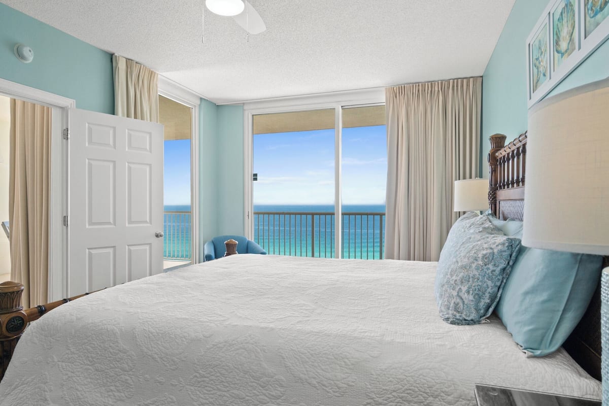 A bedroom with a large bed, a view of the ocean, and a balcony.