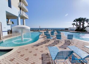 A pool area with a water fountain, lounge chairs, and a view of the ocean. - Majestic Beach Resort by Book That Condo (Panama City Beach)