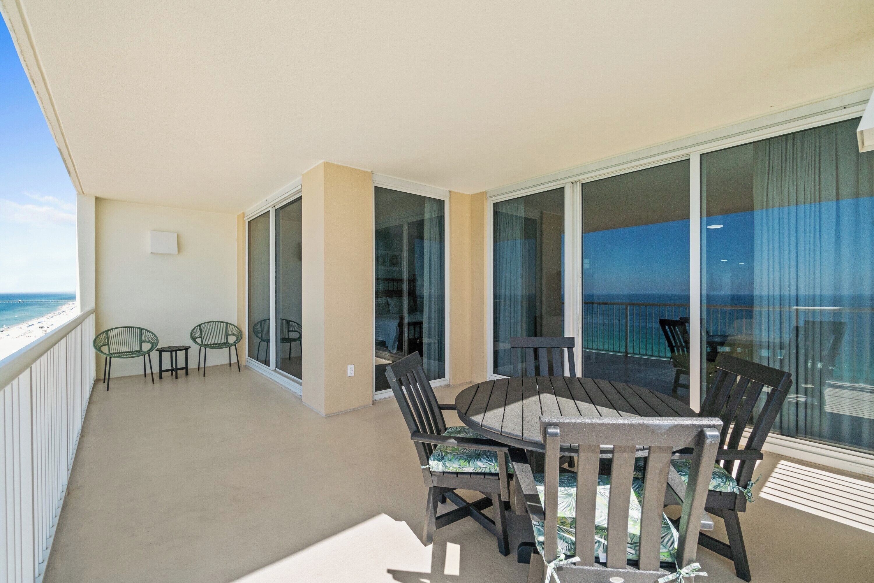 Een balkon met een tafel, stoelen, een glazen deur en uitzicht op zee.