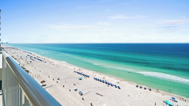 Ein Strand mit klarem türkisblauem Wasser, einem Sandufer und einem Balkon mit Blick auf die Szene.