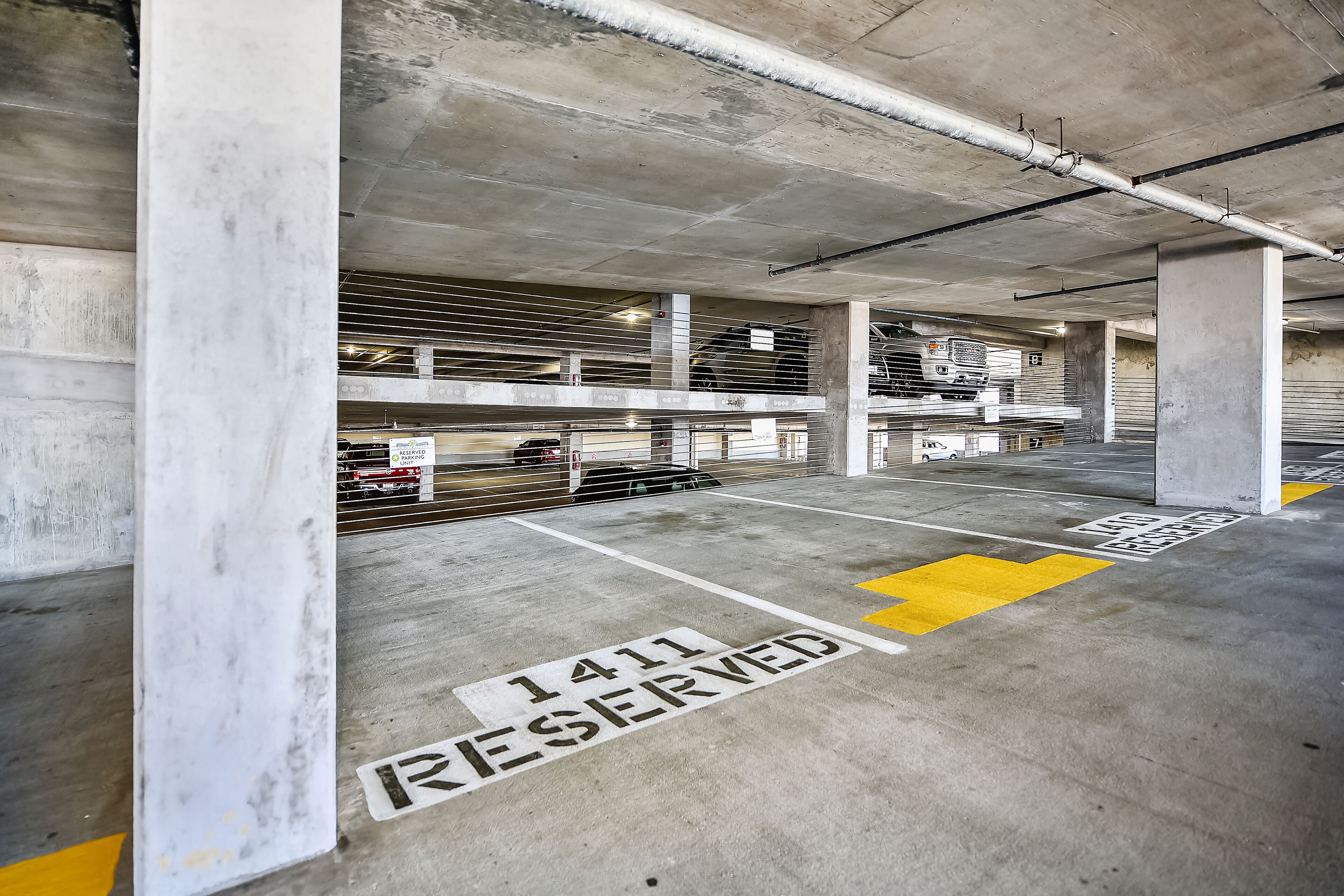 Un parking à plusieurs niveaux, doté de piliers en béton et de places de stationnement délimitées, dont une place réservée.