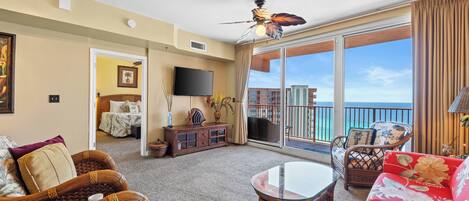 A spacious living room with a large window, a ceiling fan, and a balcony with a view of the ocean.