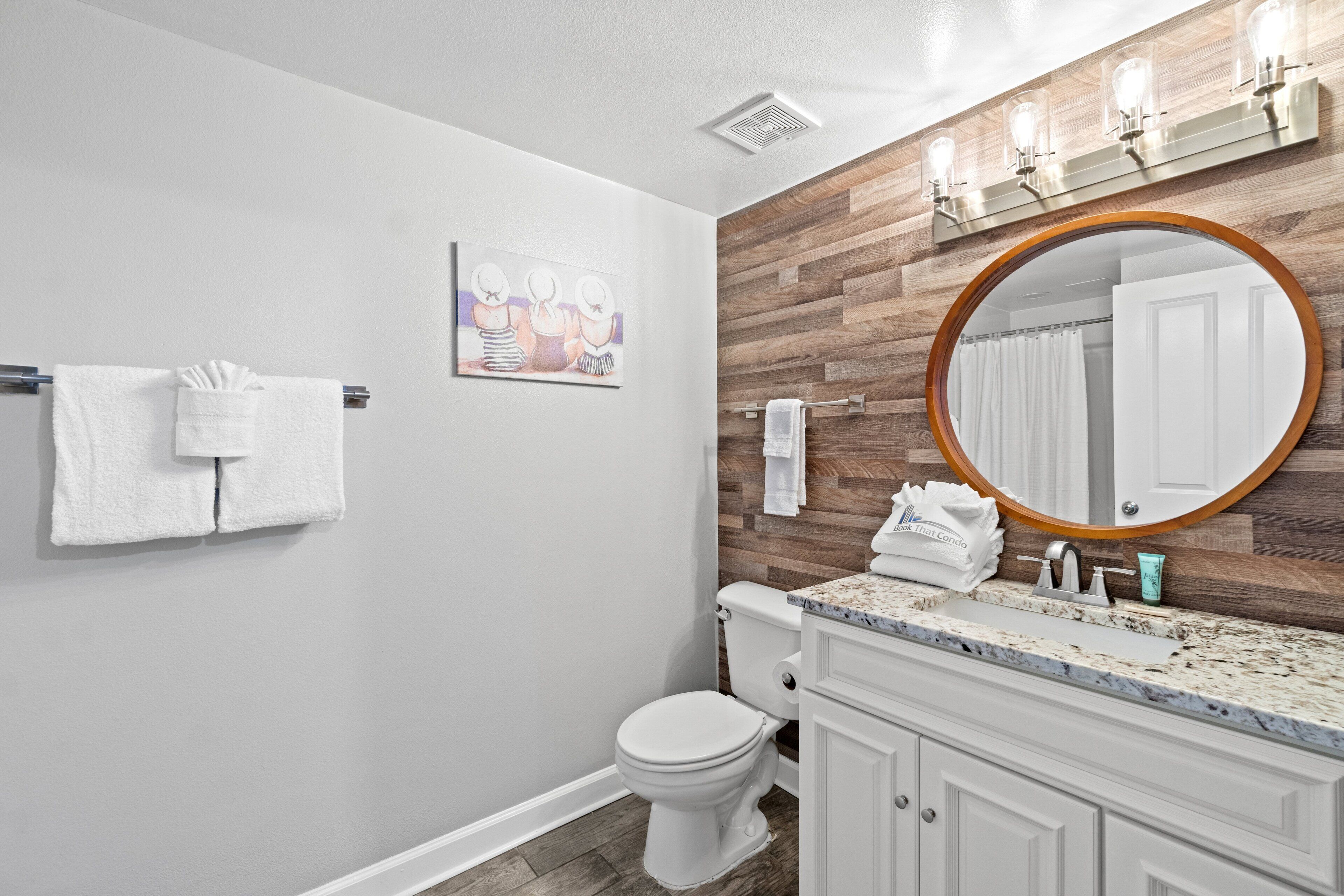 A bathroom with a white toilet, a wooden vanity with a sink, and a large mirror.