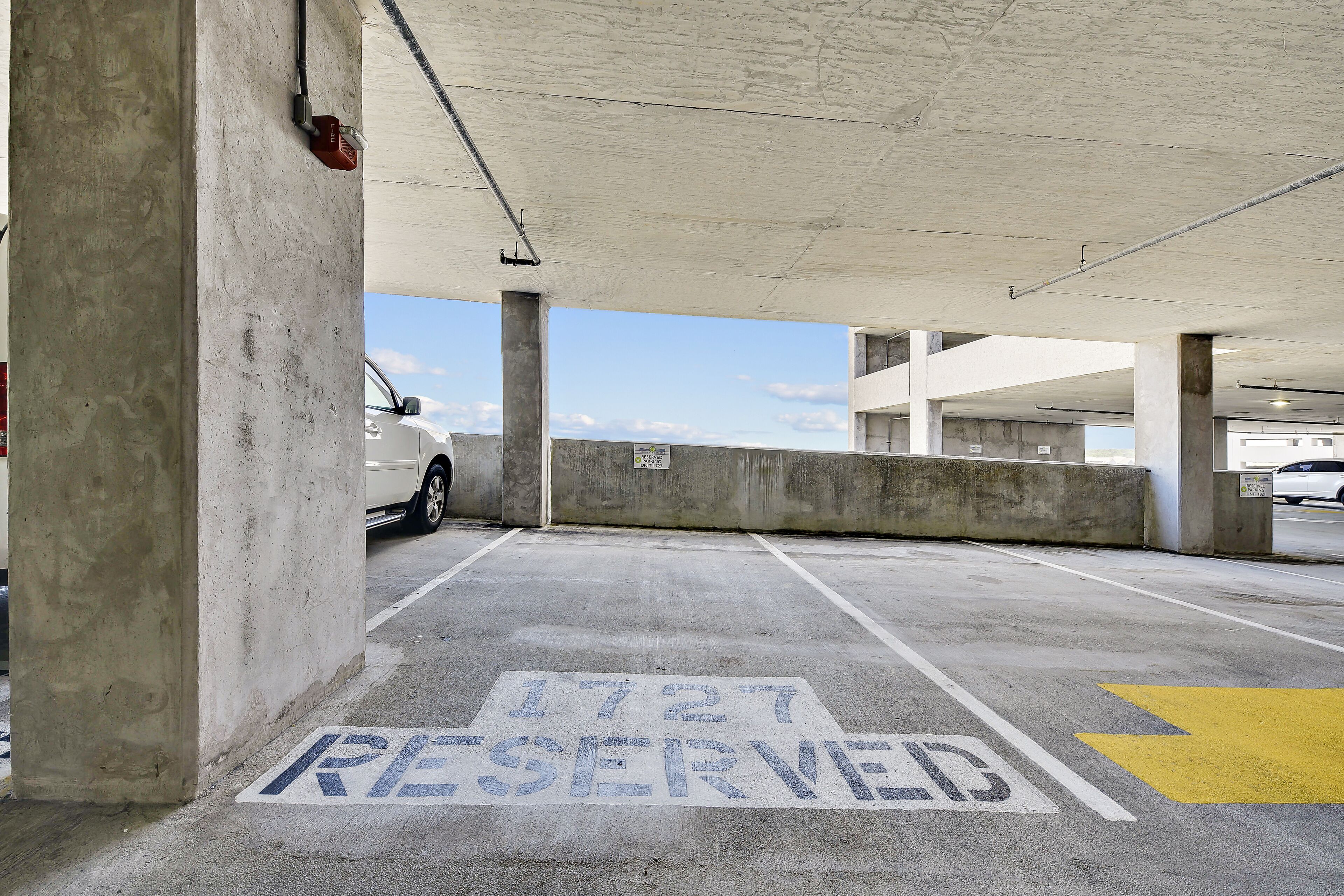 Un parking avec des piliers en béton, une voiture blanche garée et un panneau indiquant une place de stationnement réservée.