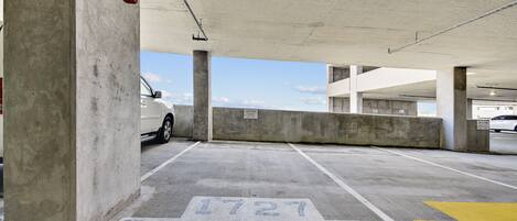Un parking avec des piliers en béton, une voiture blanche garée et un panneau indiquant une place de stationnement réservée.