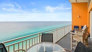 A balcony with a glass table and chairs, overlooking a turquoise sea.