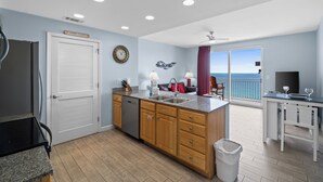 A modern kitchen with wooden cabinets, a granite countertop, and a view of the ocean through the sliding glass door.