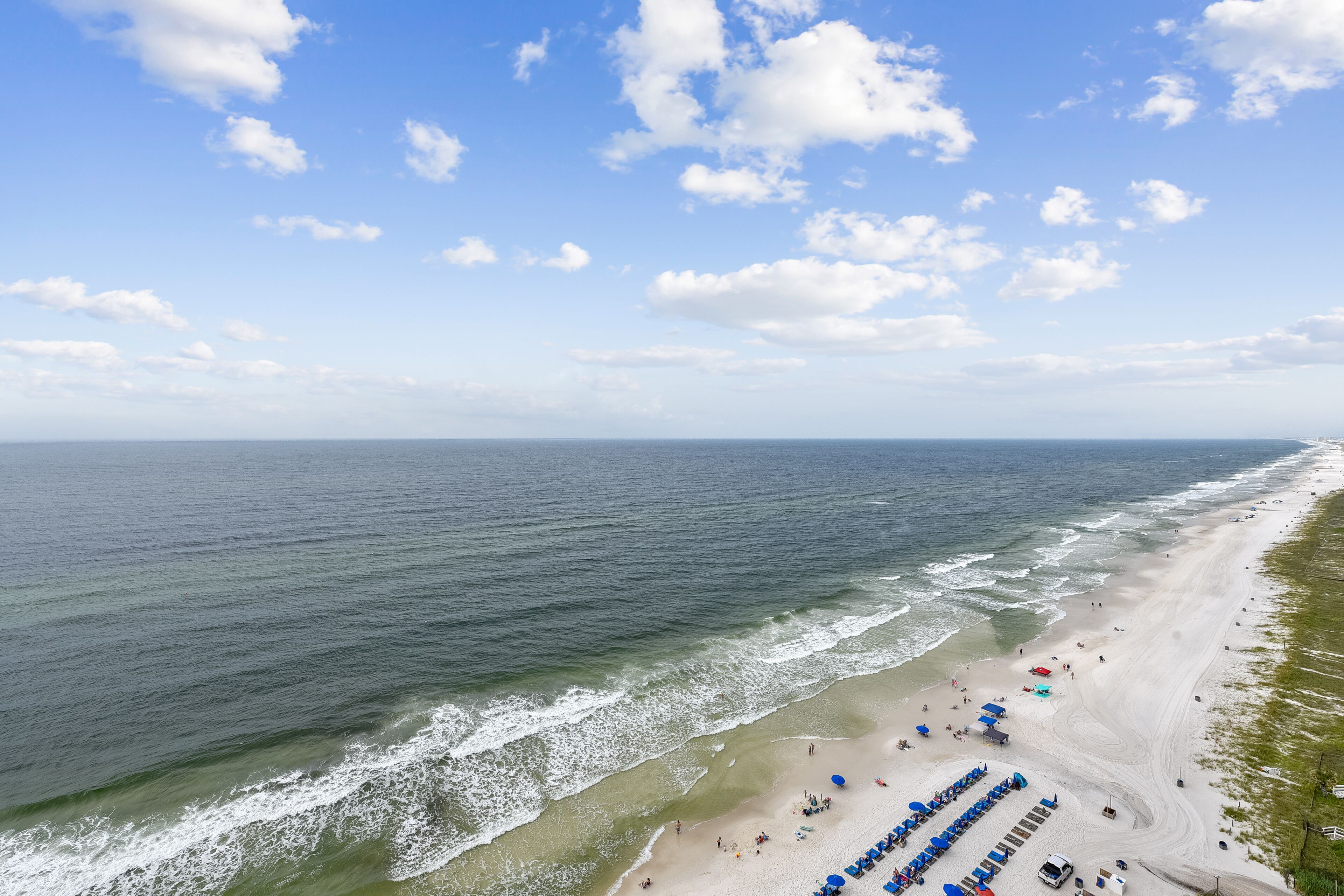 A beach with a long stretch of sand, waves, and a clear sky.