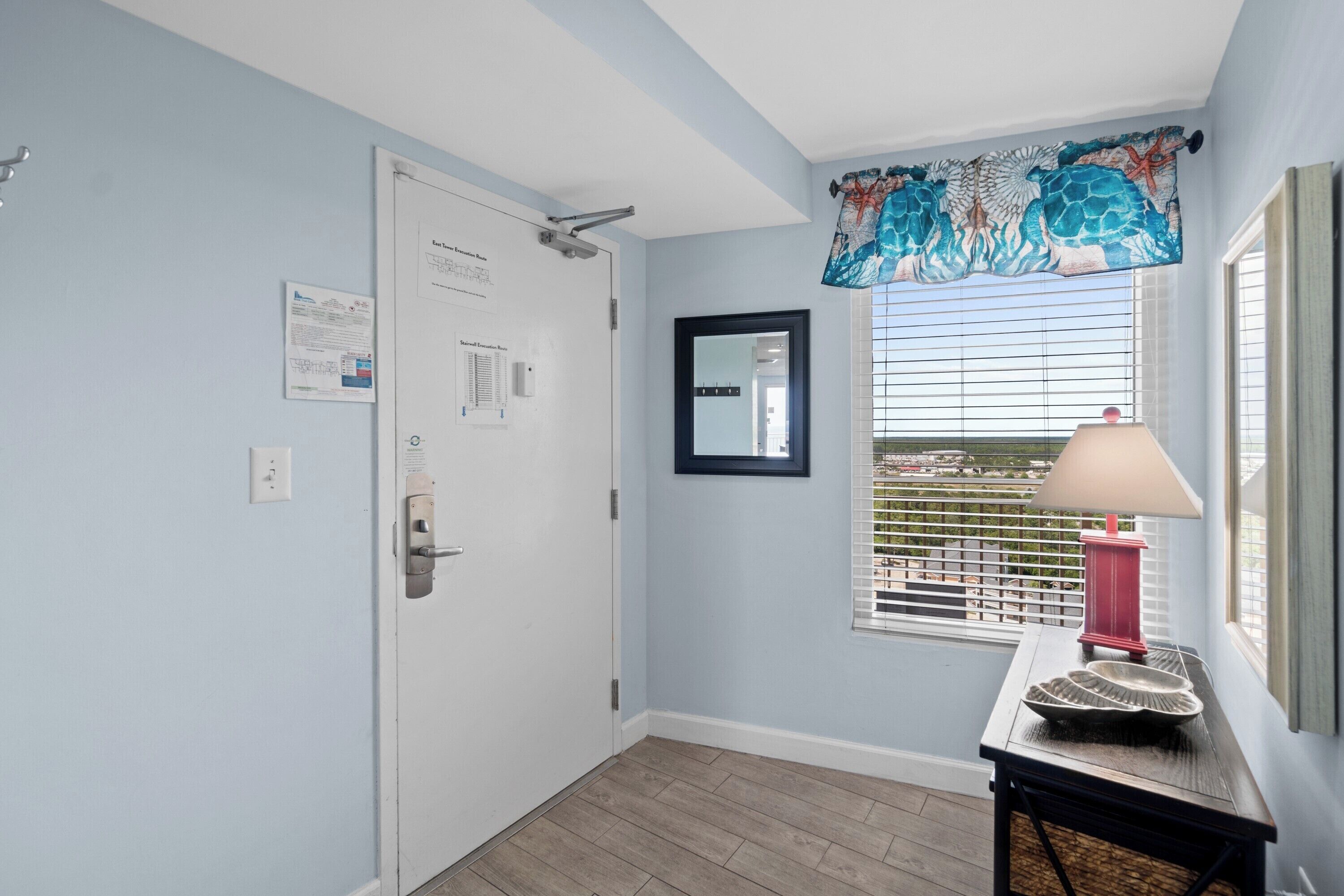 A room with a door, a window with blinds, a lamp, and a table with decorative items.