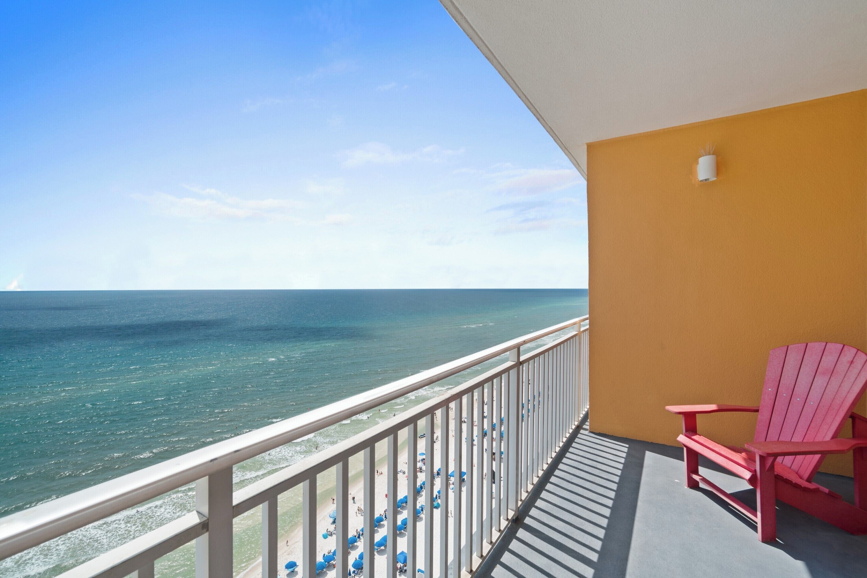 A balcony with a view of the ocean, a red chair, and a yellow wall.