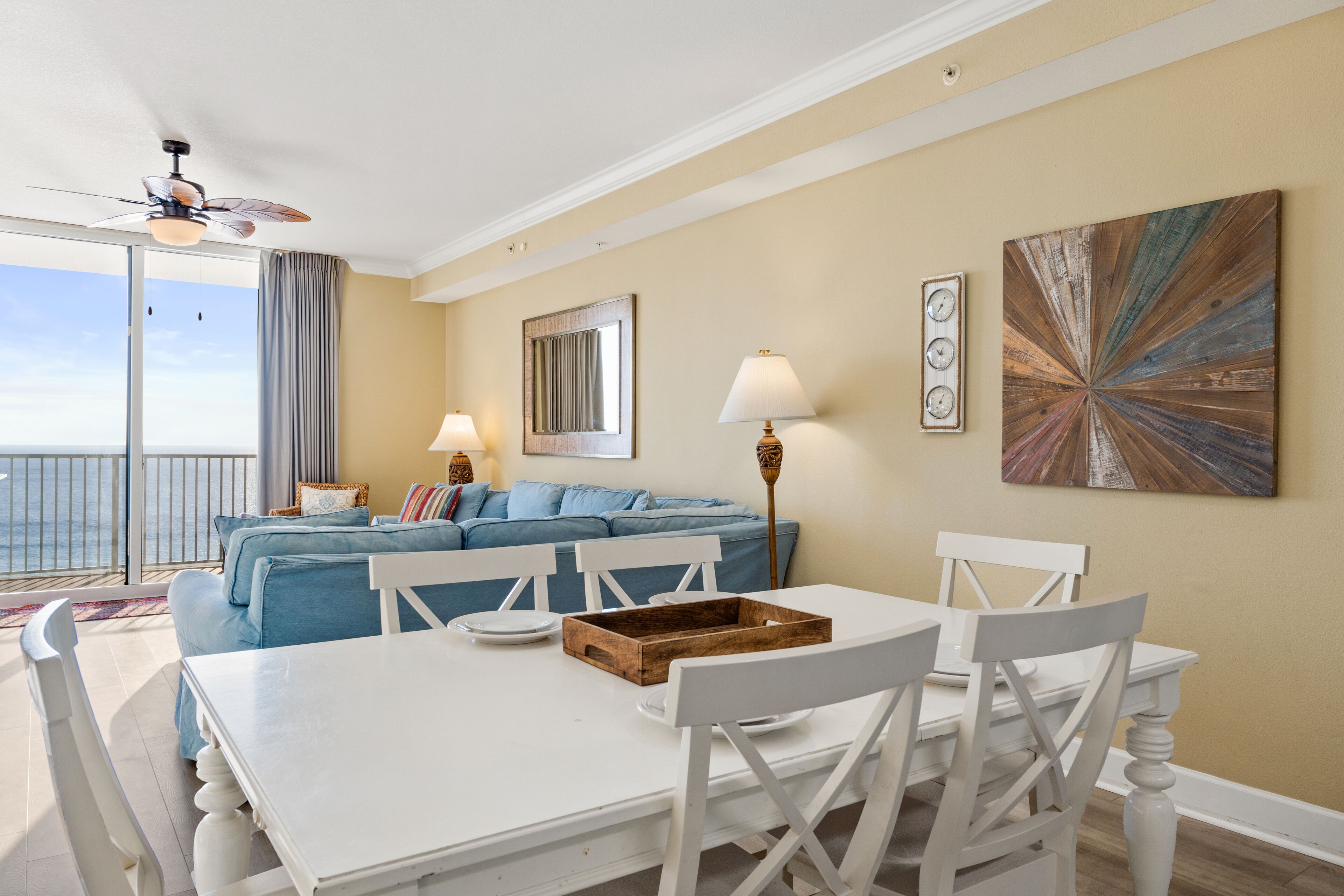 A room with a white dining table, blue sofa, and a view of the ocean.