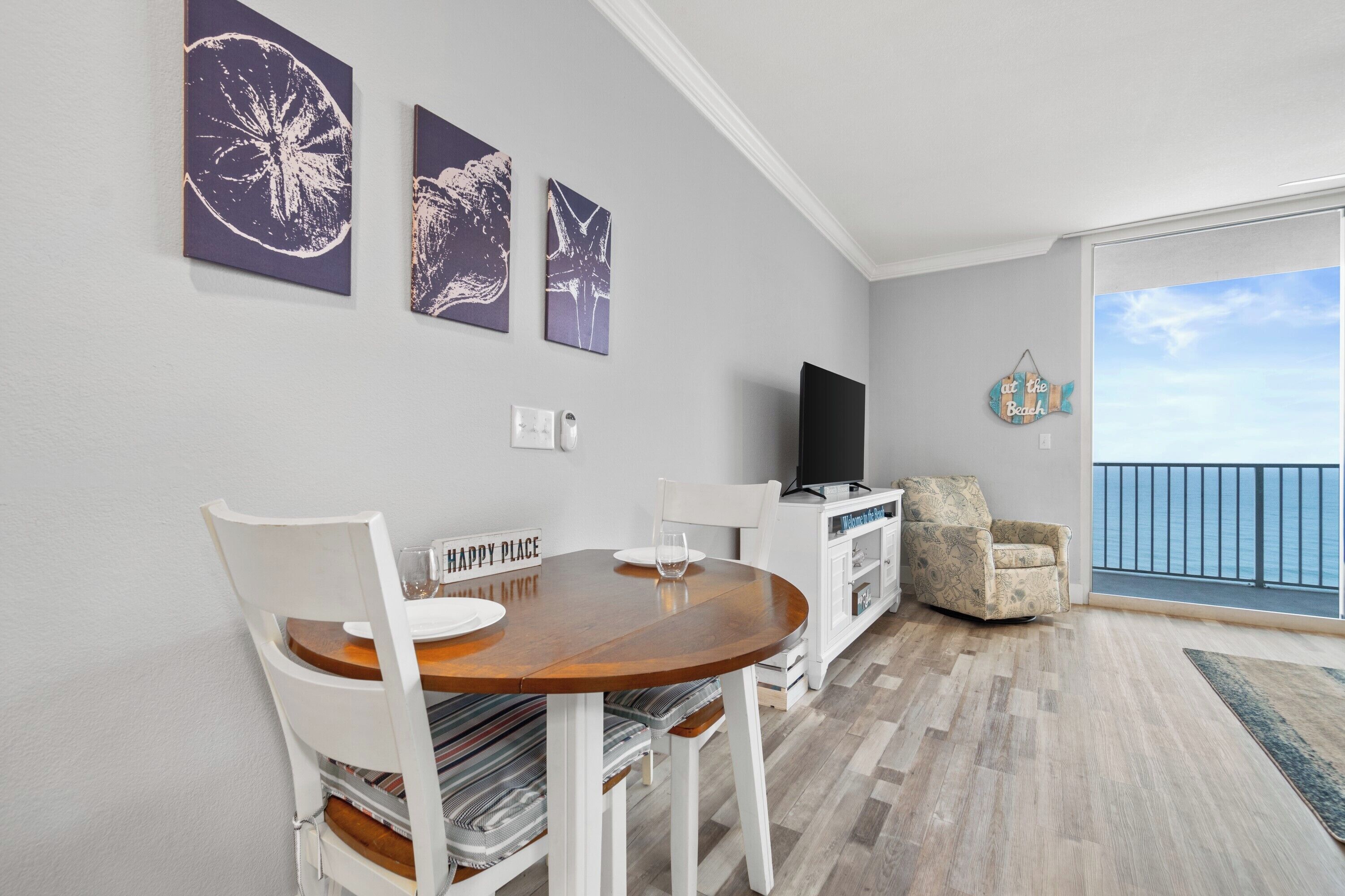 Una sala de estar moderna con una mesa de comedor, sillas blancas, un televisor de pantalla plana y obras de arte en la pared.