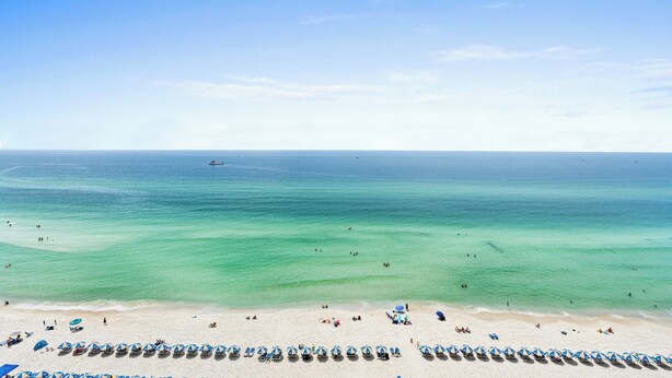 A beach with rows of umbrellas and lounge chairs along the shoreline. - Tidewater by Book That Condo (Panama City Beach)