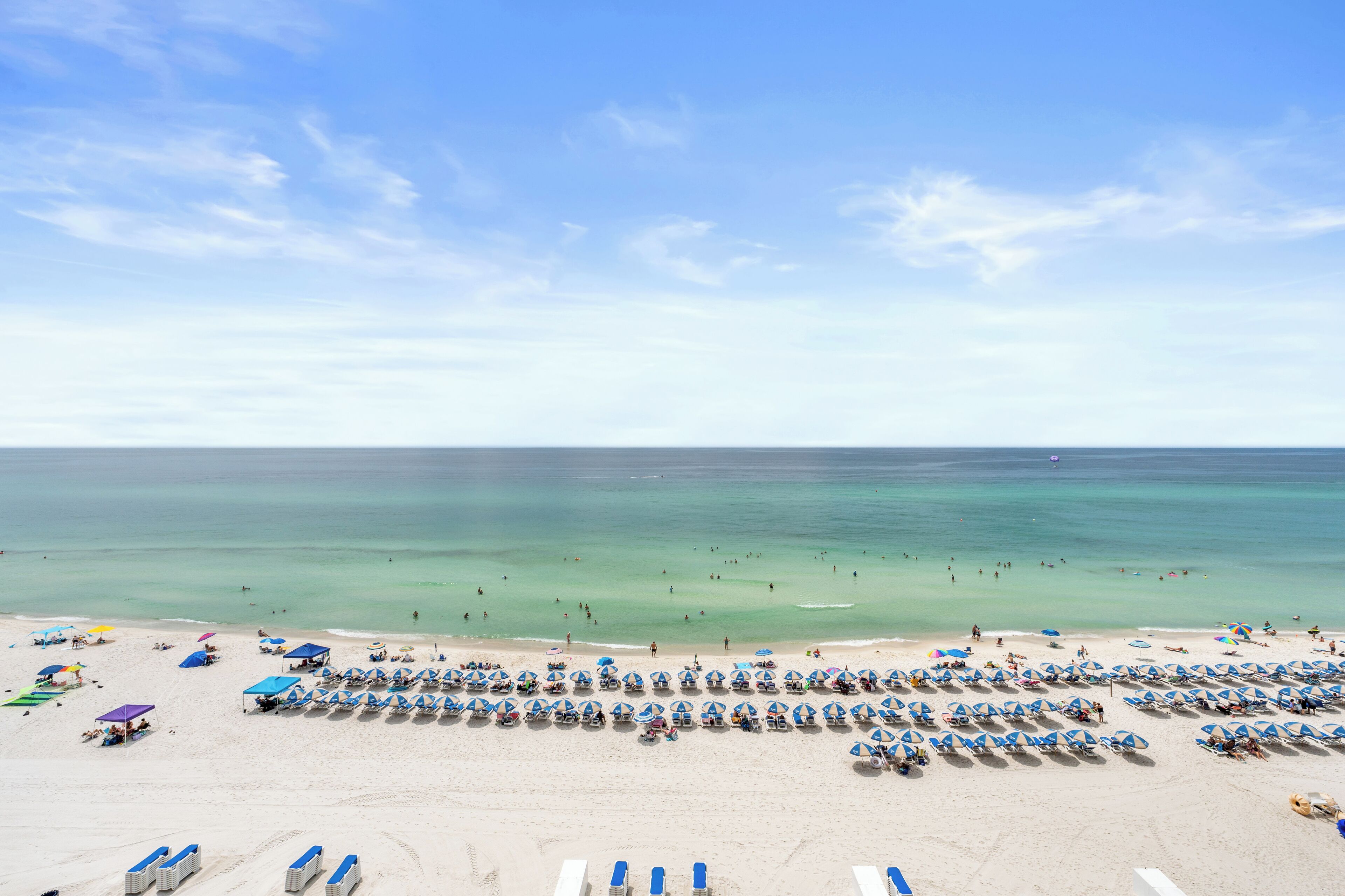 A beach with rows of sun loungers and umbrellas, a clear sky, and the ocean in the background.