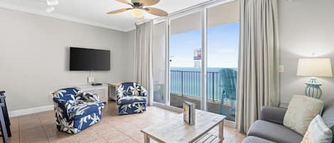 A spacious living room with a ceiling fan, a flat-screen TV, a coffee table, and two sofas.