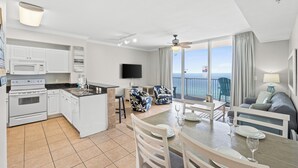 A modern kitchen with white appliances, a dining area with a table set for two, and a balcony with a view of the ocean. - Tidewater by Book That Condo (Panama City Beach)