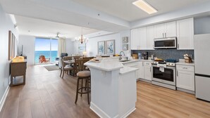 A modern kitchen with white cabinetry, a central island, and a dining area with a view. - Tidewater by Book That Condo (Panama City Beach)