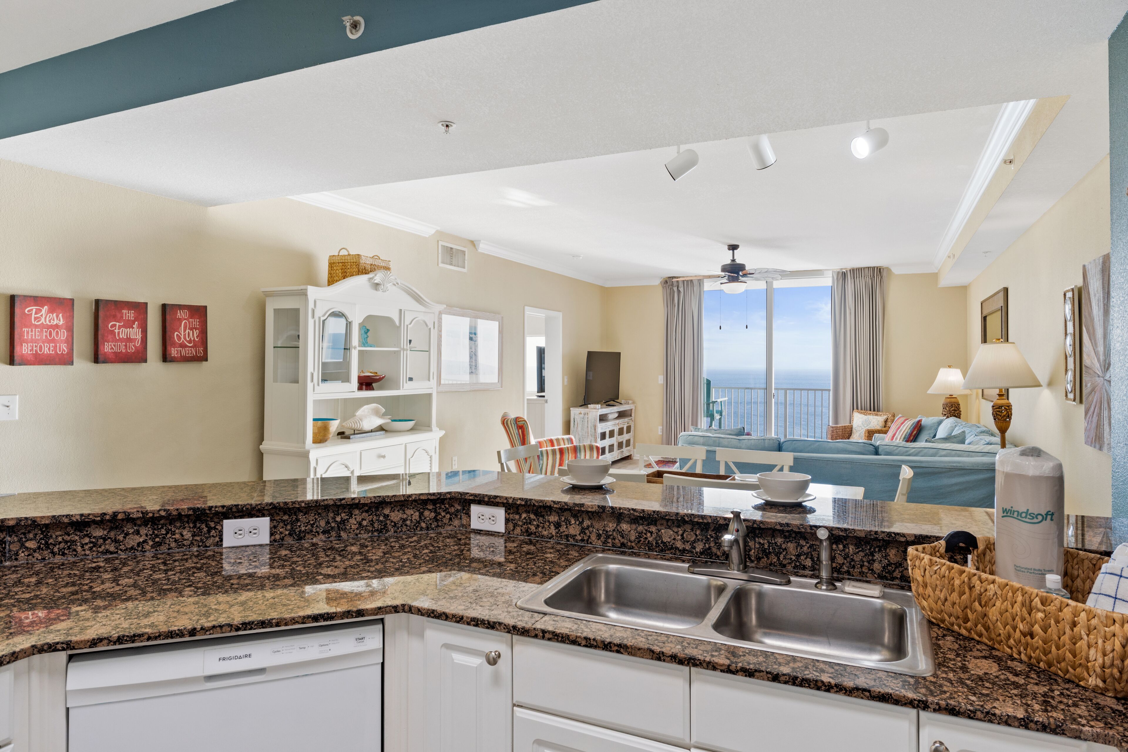 A modern kitchen with granite countertops, a built-in dishwasher, and a large window overlooking the ocean.