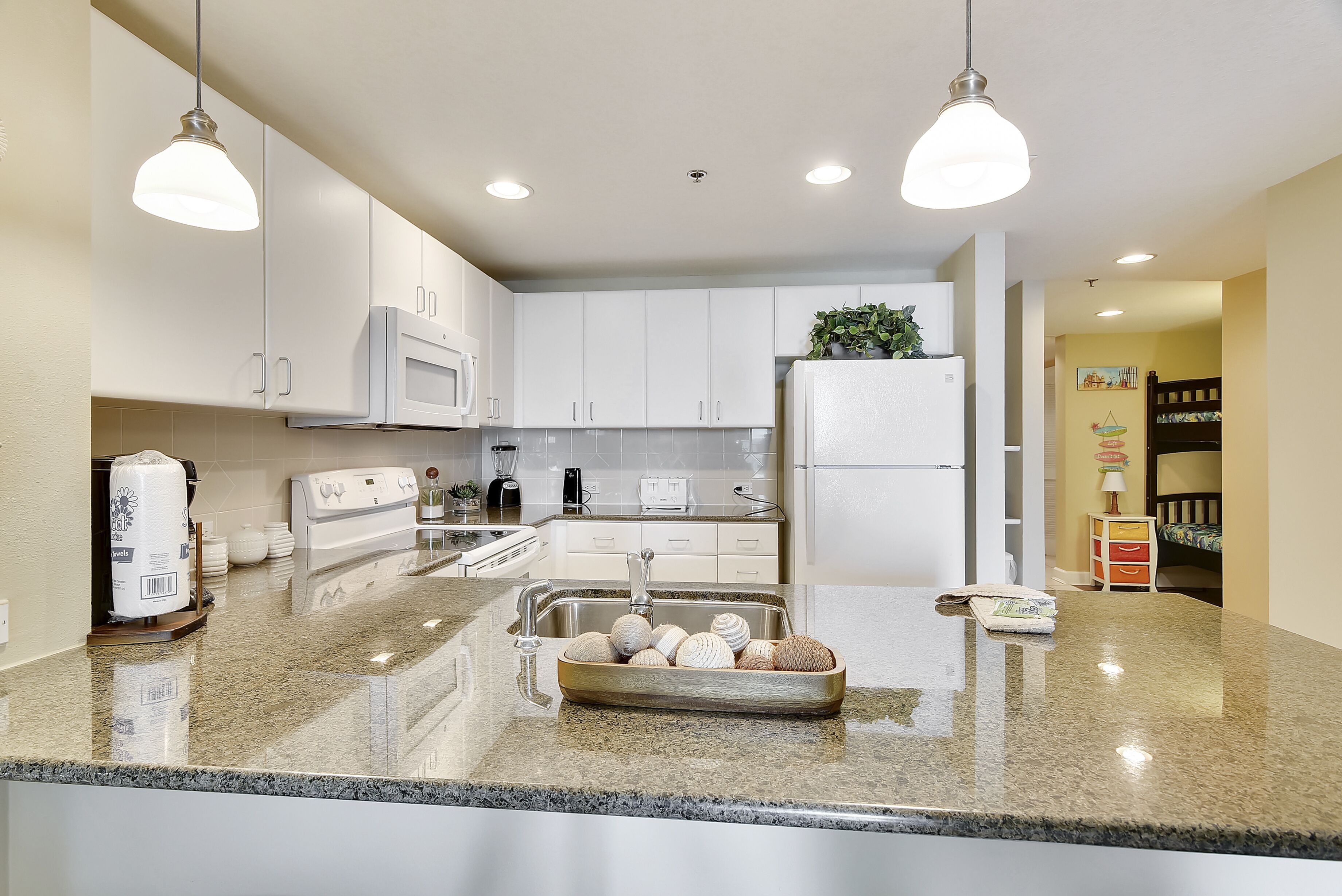 A modern kitchen with white cabinets, a granite countertop, a stainless steel sink, and a built-in microwave.