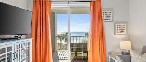 A room with a television on a cabinet, a sofa, a table, and orange curtains.