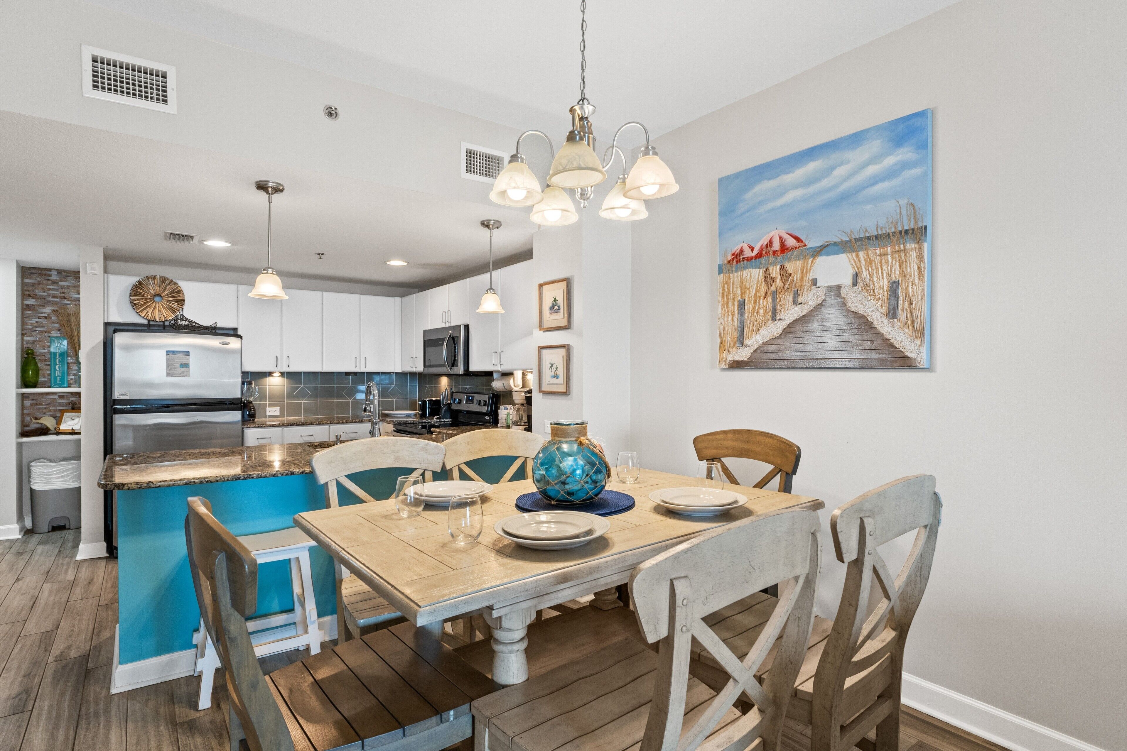 A modern kitchen with a central island, pendant lighting, and a dining area with wooden chairs and a table set for four.