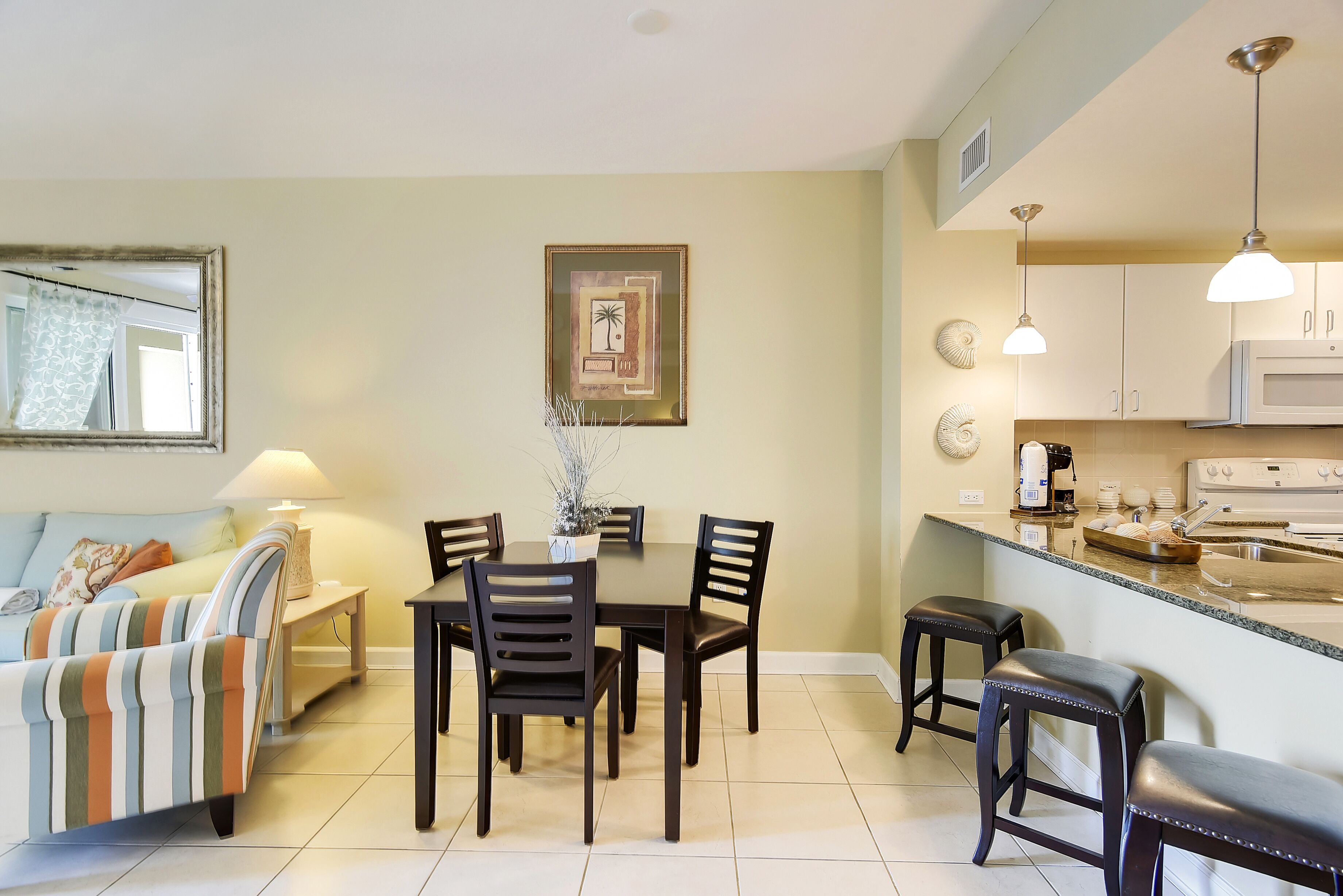 A dining area with a table and chairs, a kitchen with appliances, and a living area with a sofa and lamp.
