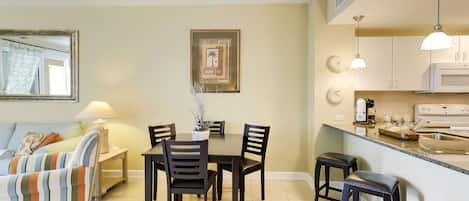 A dining area with a table and chairs, a kitchen with appliances, and a living area with a sofa and lamp.